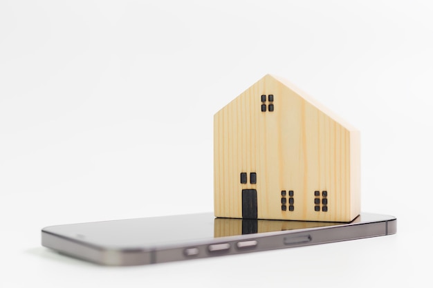 Real estate concept Home architectural wooden model over on mobile phone with white background copy space online mobile business property technology