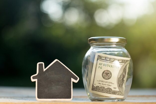 Real estate concept money jar and little house with space for text on the wooden table in the garden