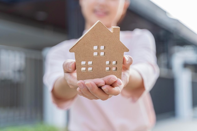 Real estate Excited young woman showing house cutout and looking at camera renting property standing on housing estate background