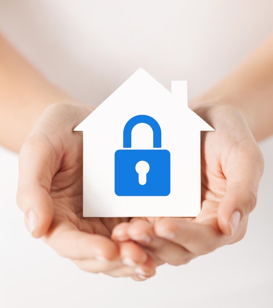 real estate and family home security concept - closeup picture of female hands holding white paper house with blue lock