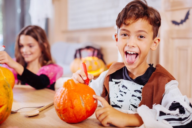 Real excitement. Cute beaming boy wearing Halloween costume showing his tongue while feeling excited