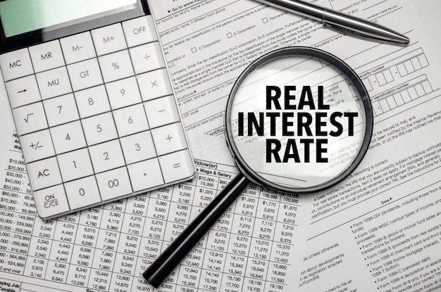 REAL INTEREST RATE words on magnifier glass and calculator with pen