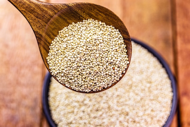 Real white quinoa in a natural wooden spoon with clay bowl. Top view