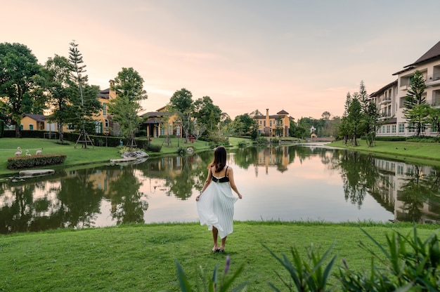 Rear of asian woman in dress standing on grass near the lake with european castle background