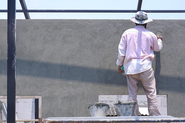 Rear side view of Asian builder on scaffolding is polishing cement wall in construction site