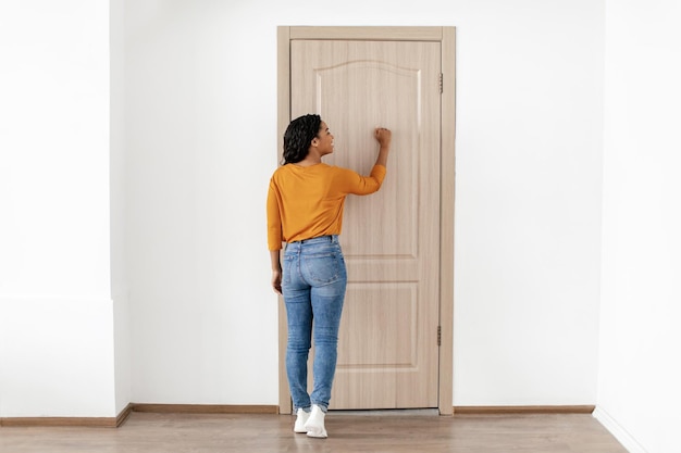 Rear view of african american lady knocking at door indoor