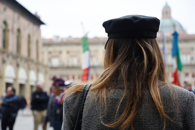 Rear view of alternative woman wearing vintage coat and sailor hat standing in a square during a political demonstration An activist women fight for women's rights Flags on background