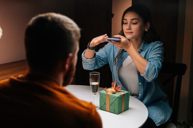 Rear view to atrractive young woman taking picture on mobile phone of gift given by boyfriend in celebration of birthday or Valentine Day