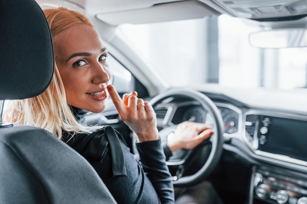 Rear view of beautiful blonde in elegant clothes that sitting inside of modern car