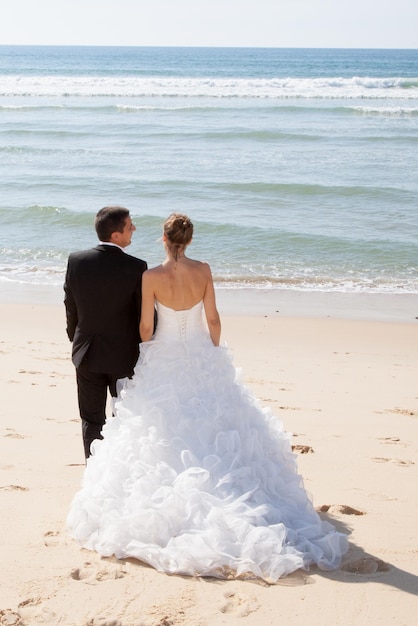 A rear view of a beautiful couple on the beach in wedding dress