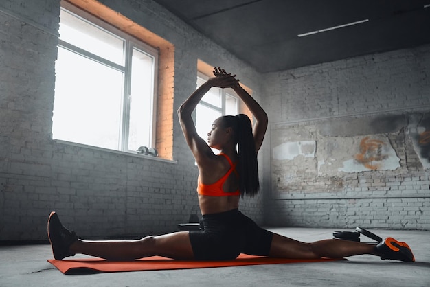 Rear view of beautiful young African woman stretching on splits in gym