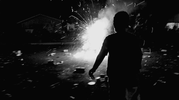 Rear view of boy in front of exploding crackers during night