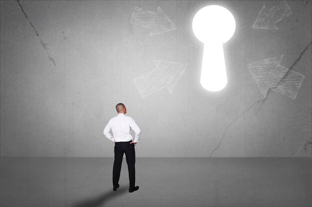 Photo rear view of businessman facing light keyhole on the wall concept of business challenge