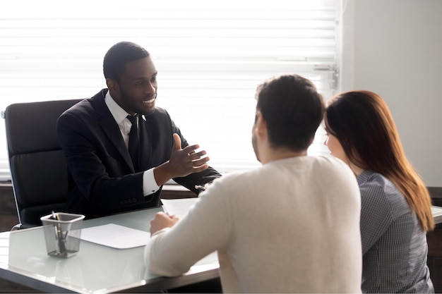 Rear view couple during meeting with African ethnicity family lawyer spouses and realtor negotiating about rental property banker worker consulting first realestate purchasing lease mortgage concept