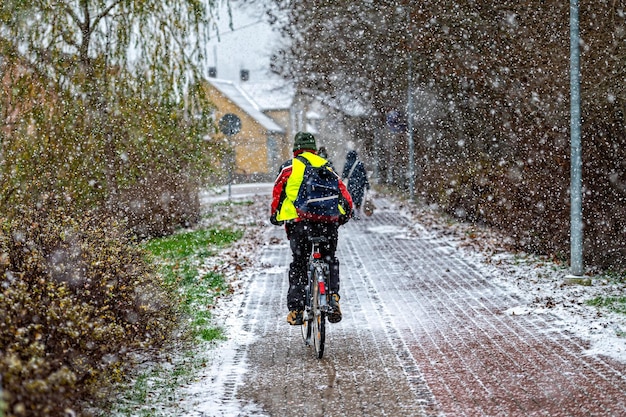 Rear view of a cyclist riding on a paved sidewalk during a snowfall