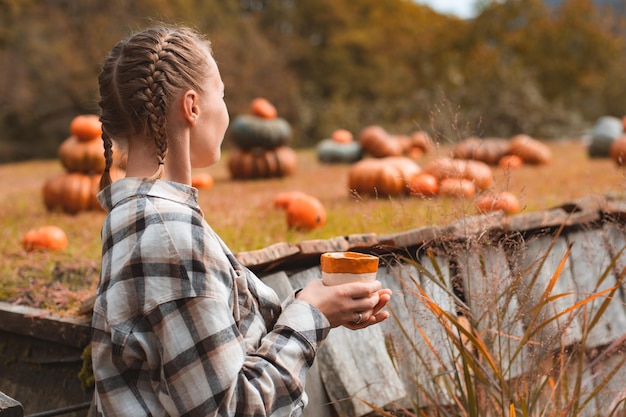 Rear view of a farmer's woman with a drink mug looking at pumpkins in a pumpkin field against the background of mountains