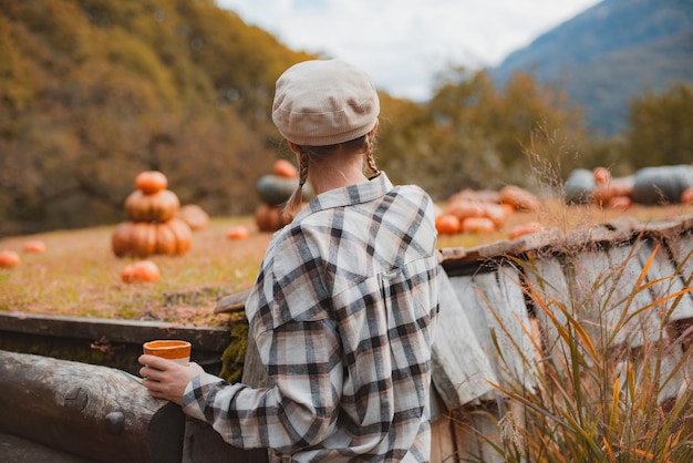 Rear view of a farmer's woman with a drink mug looking at pumpkins in a pumpkin field against the background of mountains