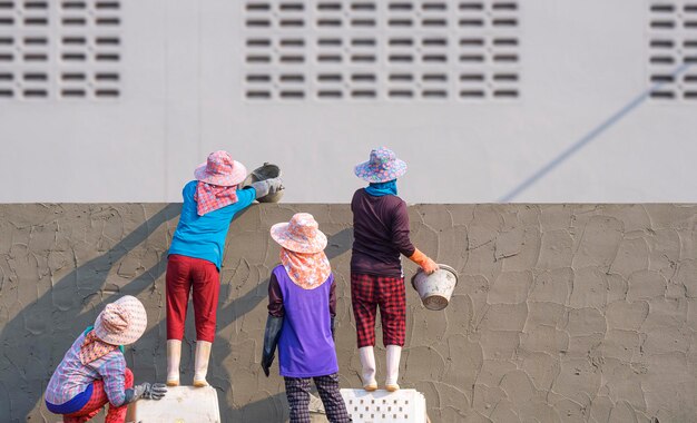 Rear view of Female Construction Laborer Group Plastering Cement on Fence Wall outside of Building