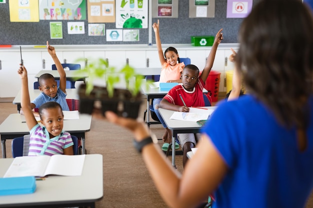 Rear view of female teacher holding plant seedlings while teaching in the class at elementary school