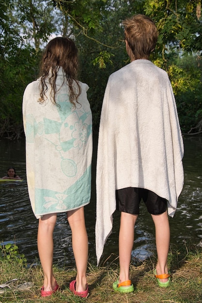 Photo rear view of friends with towels standing against lake