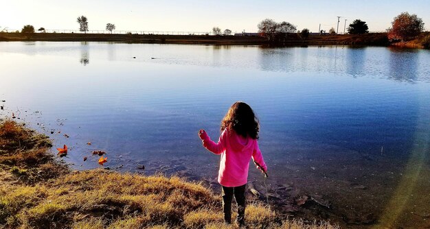 Photo rear view of girl standing at lakeshore against sky