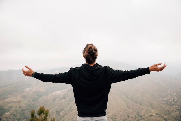 Rear view of a male hiker outstretching their arms looking at mountain landscape