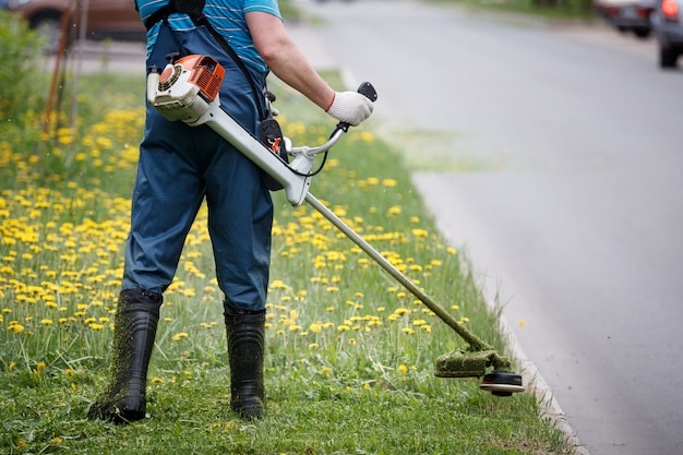 Rear view of a man in overalls with a gas mower mowing grass on the lawn 