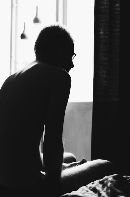 Rear view of man sitting on bed at home