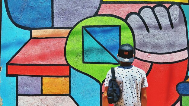 Rear view of man standing by graffiti wall