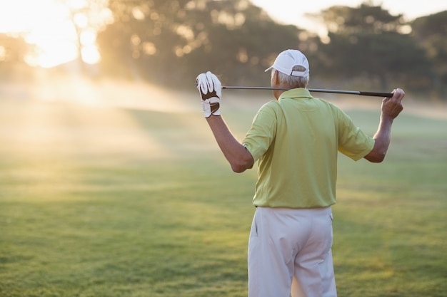 Rear view of mature golfer carrying golf club