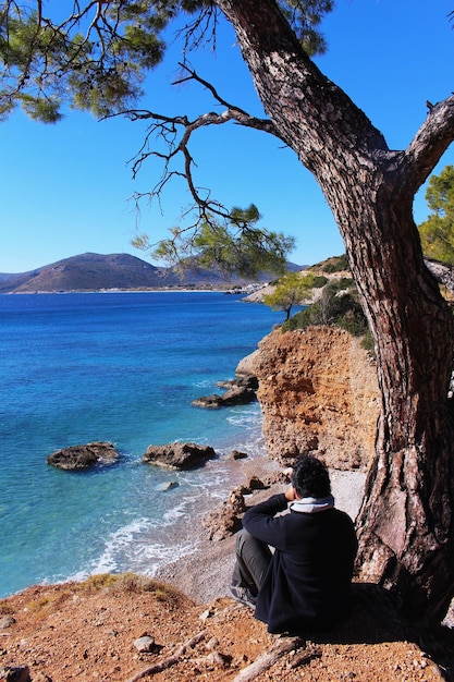 Photo rear view of mid adult man sitting at beach against clear sky during sunny day