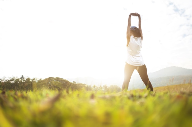 Rear view of mid adult woman exercising while standing on grassy field against sky