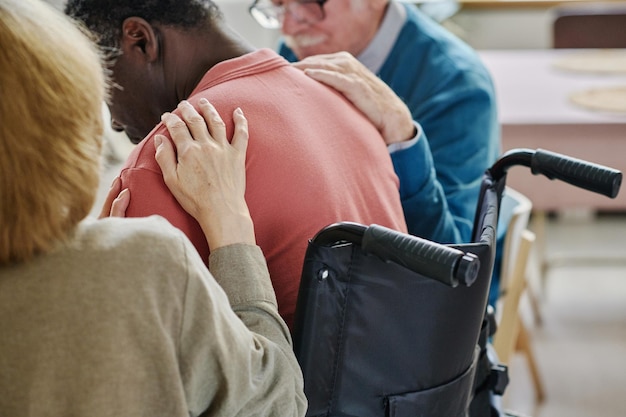 Rear view of people supporting man in depression sitting in wheelchair they visiting therapy