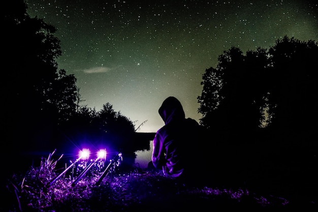 Photo rear view of person sitting by illuminated lights against sky at night