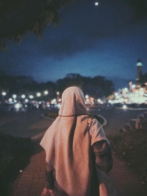 Rear view of person standing on illuminated land against sky at night