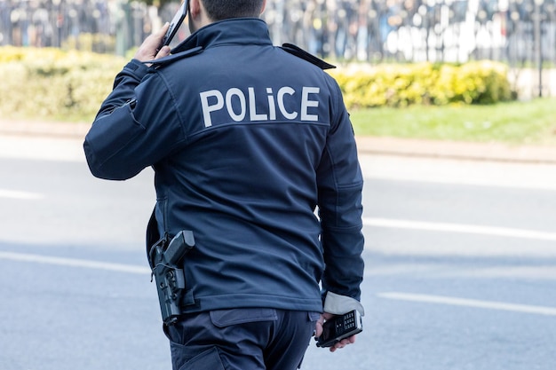 Rear View Of Police Man Using Smart Phone On City Street