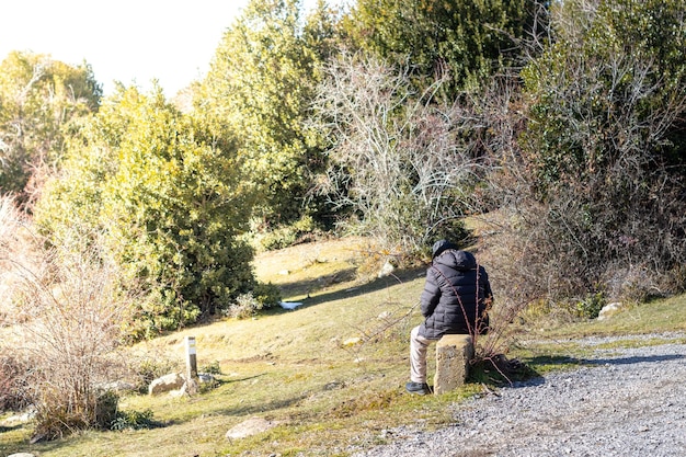 Rear view of senior man sitting in the field Traveler man sitting back surrounded by bushes