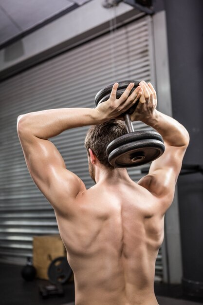 Rear view of shirtless man lifting heavy dumbbell at the crossfit gym