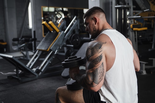 Rear view shot of a big muscular man resting at gym holding heavy dumbbells copy space