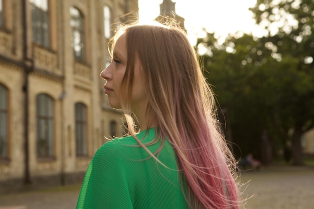 Rear view shot of a lovely young woman with pink hair walking in the city on sunset