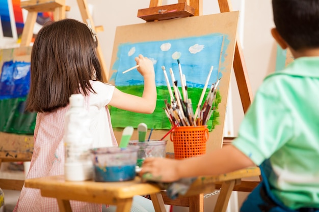 Rear view of some kids working on a painting and drawing some clouds for art class