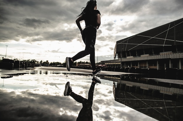 Rear view of strong athletic woman runner in motion. Morning workouts outdoors after the rain. Woman preparing for a marathon.