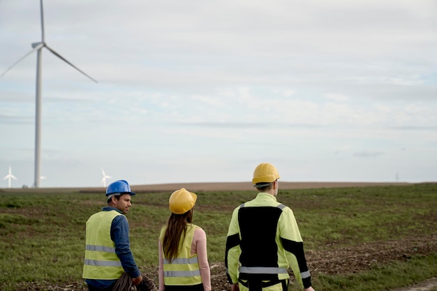 Photo rear view of team of caucasian and latin engineers walking across wind turbine field and discussing