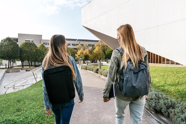 Rear view of two college classmates walking together and chatting on campus.