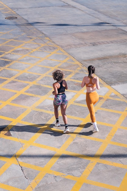 Rear view of two friends running along city road