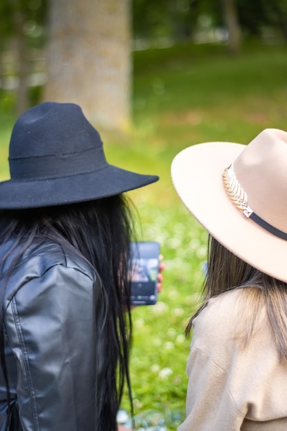 Rear view of two girls looking at the screen of the phone Back view of two girls in hats looking at the cell phone screen Concept of two teenage girls looking at the screen of the smart phone