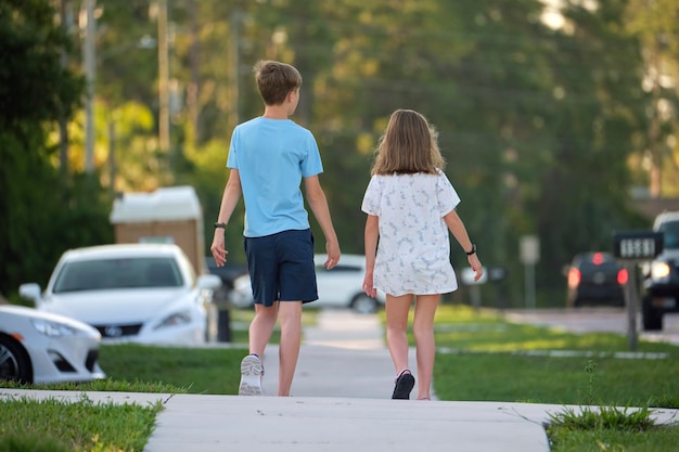 Rear view of two young teenage children girl and boy brother and sister walking together on rural street on bright sunny day Vacation time concept