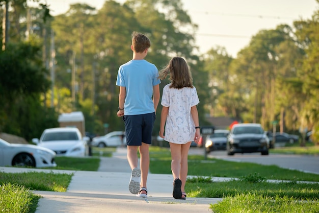 Rear view of two young teenage children girl and boy brother and sister walking together on rural street on bright sunny day Vacation time concept