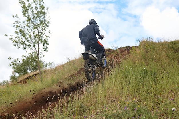 Rear view of unrecognizable motorcyclist in jacket climbing hill trail outdoors