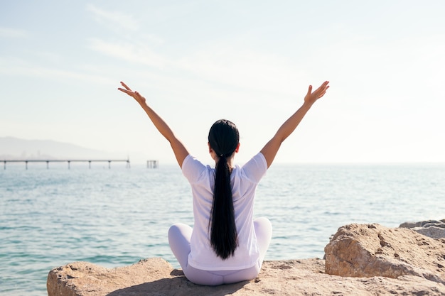 Rear view of an unrecognizable young woman sitting doing yoga by the sea, concept of spirituality and relax